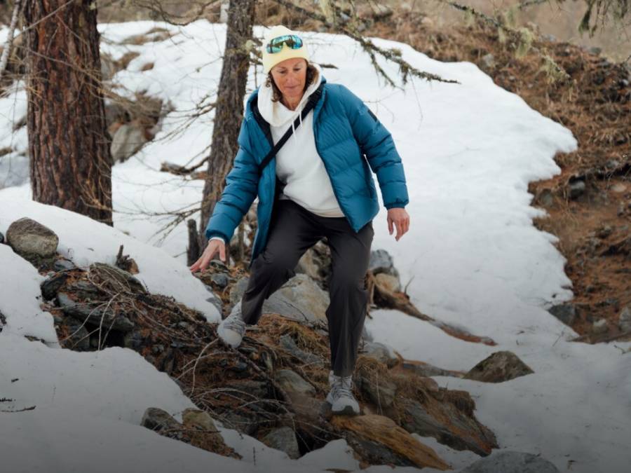 Dwa sanki z dwiema osobami na każdym zjeżdżają po ośnieżonym stoku. Osoby śmieją się i mają na sobie zimowe ubrania, czapki i okulary przeciwsłoneczne; w tle widać ośnieżone góry.