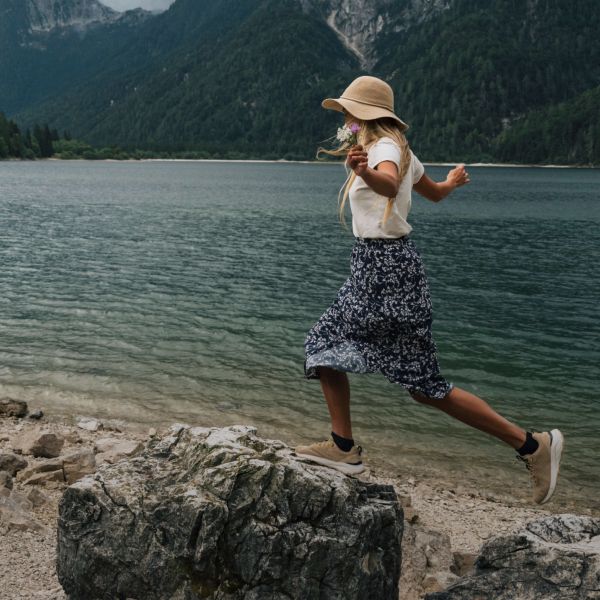 Kobieta w letnim outdoorowym ubraniu balansuje na kamieniach nad morzem