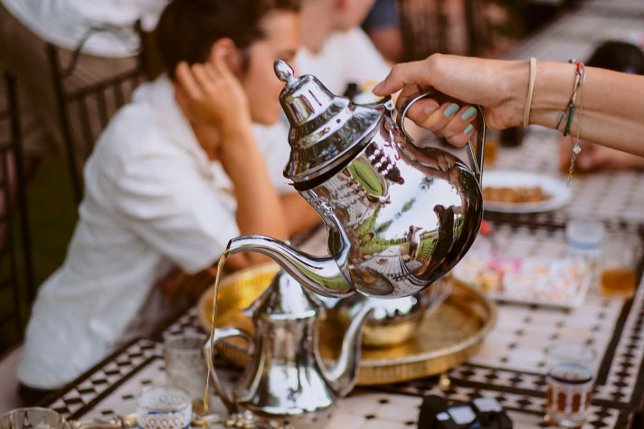 Osoba rozlewa herbatę ze srebrnego czajniczka