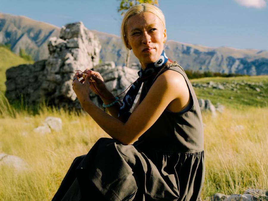 Blondynka siedzi na zielonej łące i patrzy w dal, otoczona górami