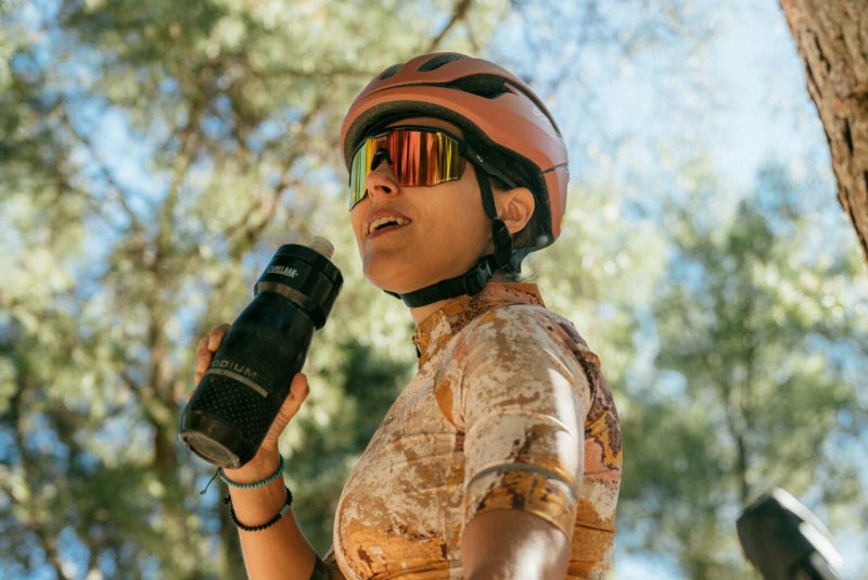 Kobieta w kasku rowerowym pijąca wodę z butelki