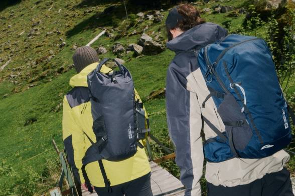 Dwoje wędrowców od tyłu z plecakami na plecach idzie przez drewniany&nbsp;most