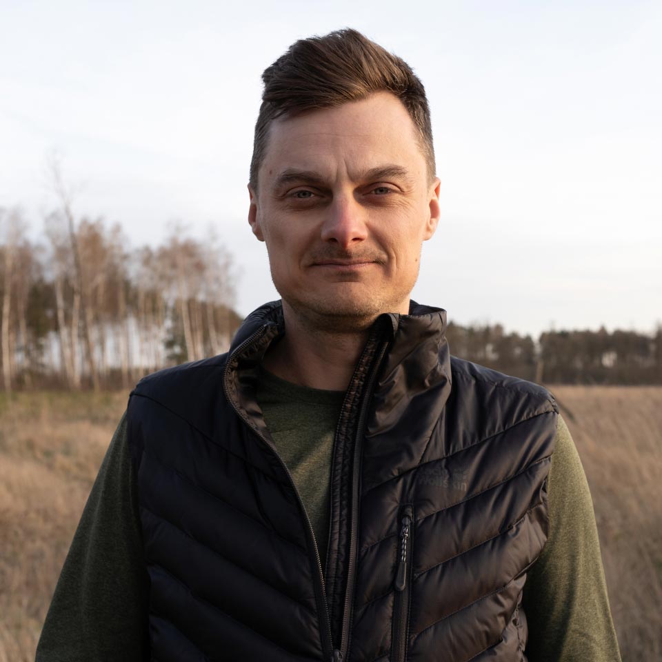 Mężczyzna z krótkimi włosami, poważnie patrzący w obiektyw, ubrany w kamizelkę.