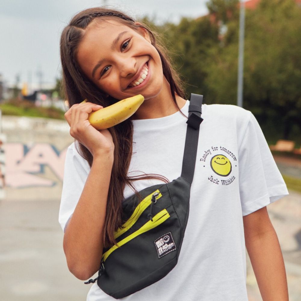 Dziewczynka uśmiecha się do obiektywu i trzyma banana przy uchu