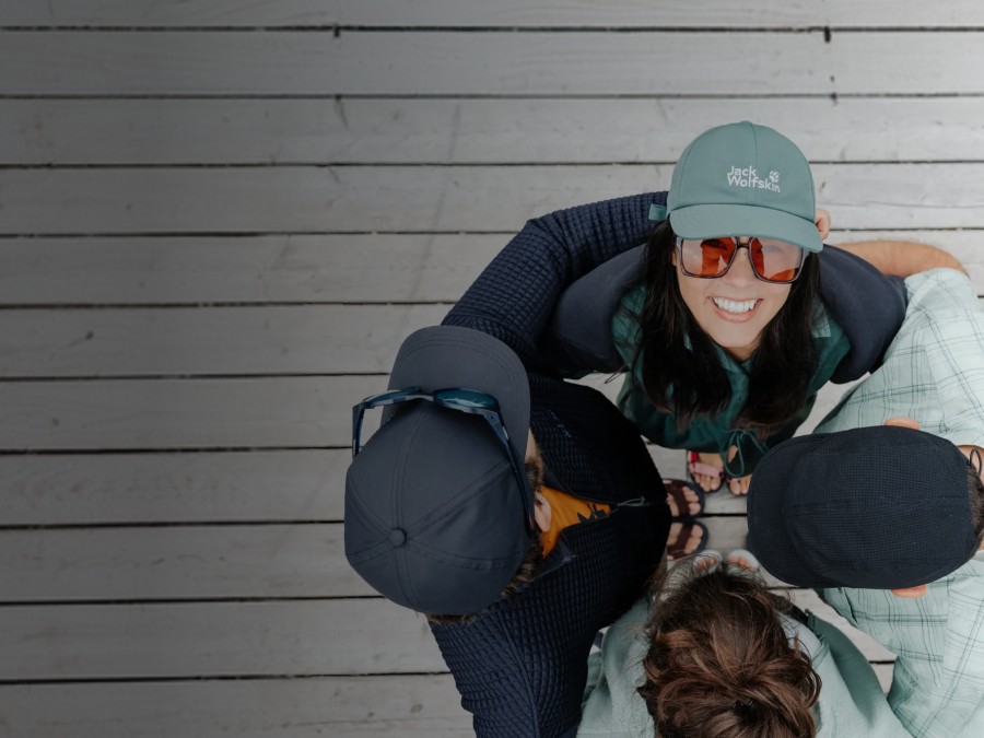 Dwa sanki z dwiema osobami na każdym zjeżdżają po ośnieżonym stoku. Osoby śmieją się i mają na sobie zimowe ubrania, czapki i okulary przeciwsłoneczne; w tle widać ośnieżone&nbsp;góry.