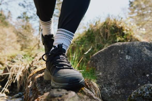 Zbliżenie na osobę w butach na wędrówki idącą przez głaz